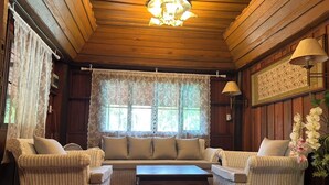 A cozy room with a wooden ceiling, a large window with lace curtains, wicker furniture, and a table. - Blooming Village by Aforetime (Koh Samui)