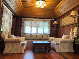Una habitación acogedora con techo de madera, un ventanal con cortinas de encaje, muebles de mimbre y una mesa.