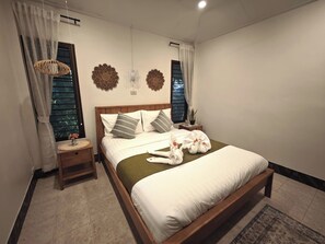 Una cama bien tendida con almohadas, una mesita de noche con lámpara y decoración en la pared.