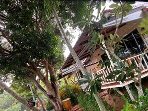 A two-story building with a balcony, surrounded by dense foliage. - Blooming Village by Aforetime (Koh Samui)