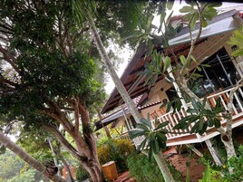 Un edificio de dos plantas con balcón, rodeado de abundante follaje.