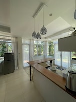 Una cocina moderna con una isla central, luces colgantes y ventanas amplias.