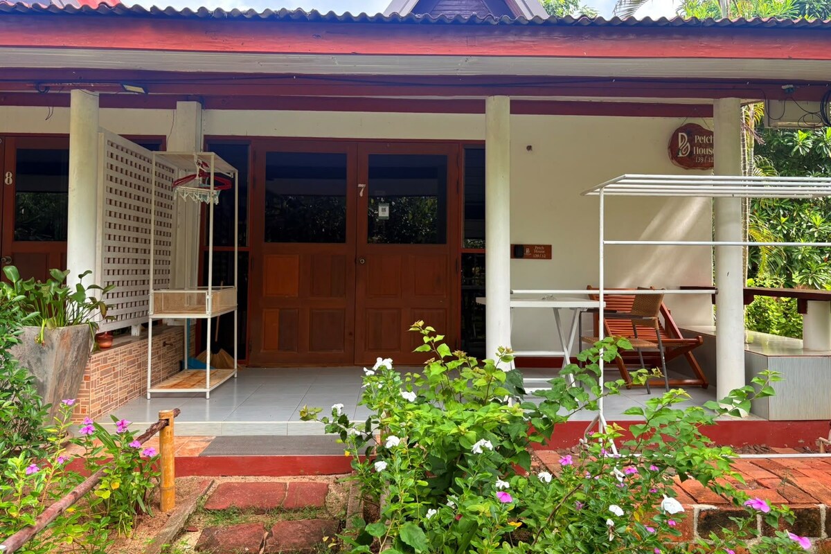 A two-story building with a red roof, a wooden door, and a balcony with a white railing.