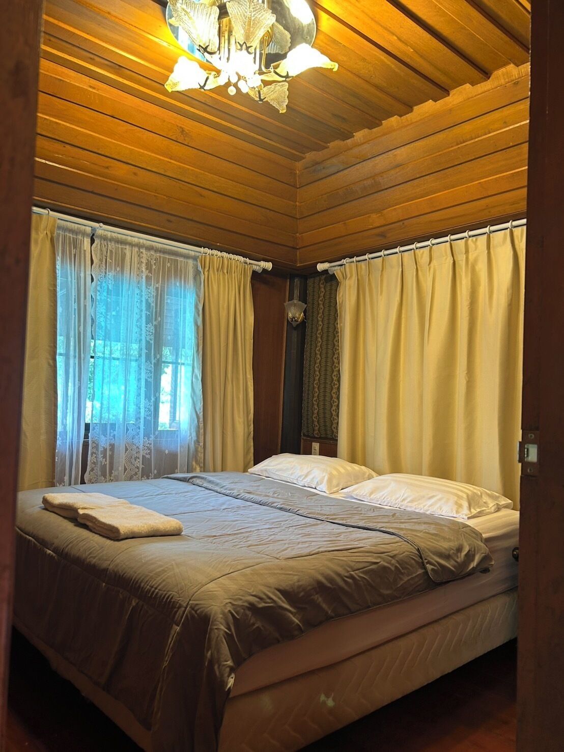 A wooden-paneled room with a bed, curtains, and a chandelier.