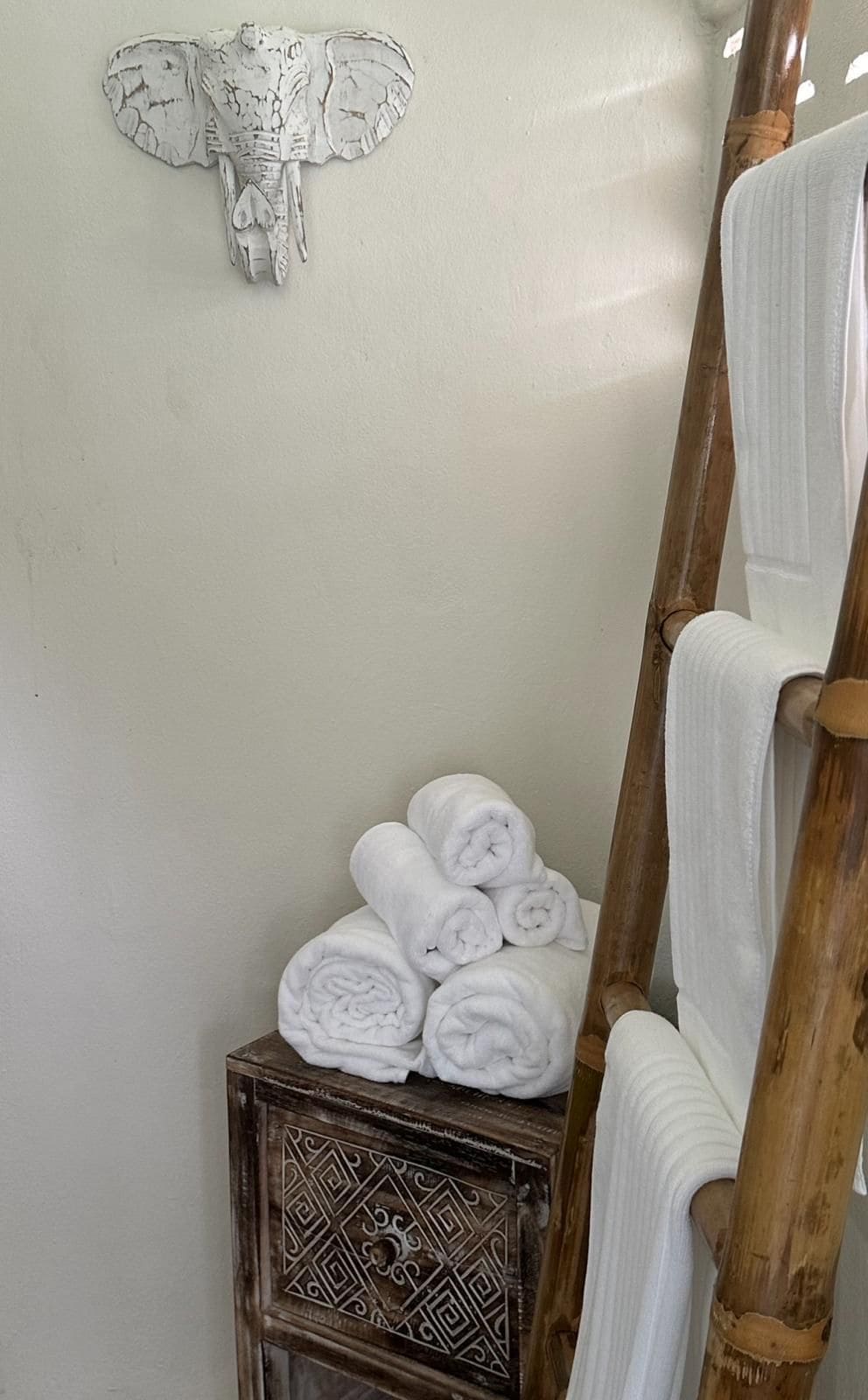 A bathroom with a wooden bench, towels, and a decorative wall piece.
