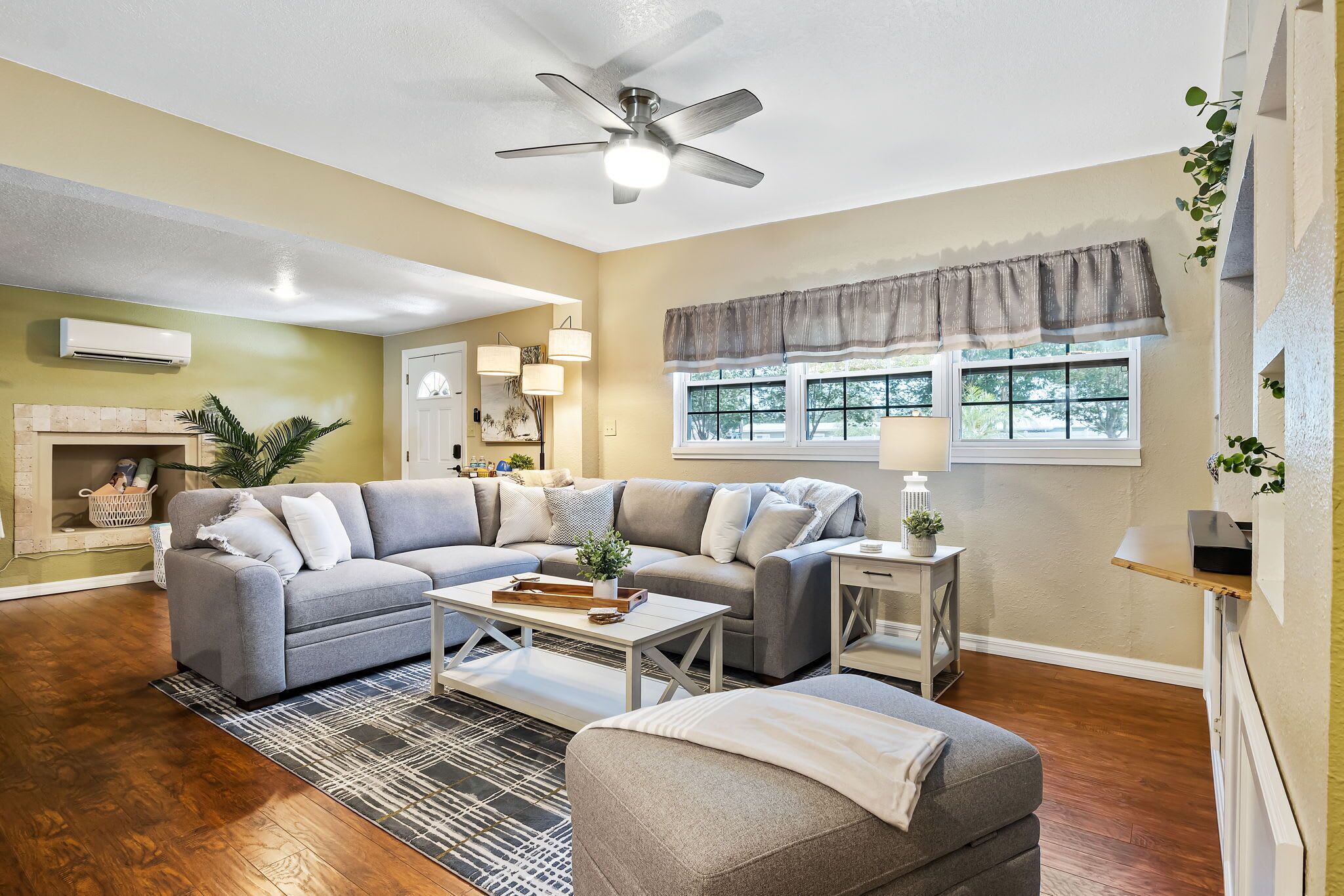 A living room with a gray sectional sofa, a white coffee table, and a gray armchair. There is a fireplace with a white mantel and a ceiling fan.