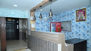 A reception area with a wooden reception desk, two hanging pendant lights, a wall-mounted fan, and a Coca-Cola refrigerator. - Hotel Ankitha Grand (Hyderabad)