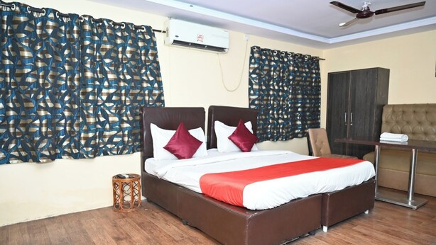 A neatly made bed with a red blanket, a wooden floor, and a ceiling fan. - Hotel Ankitha Grand (Hyderabad)
