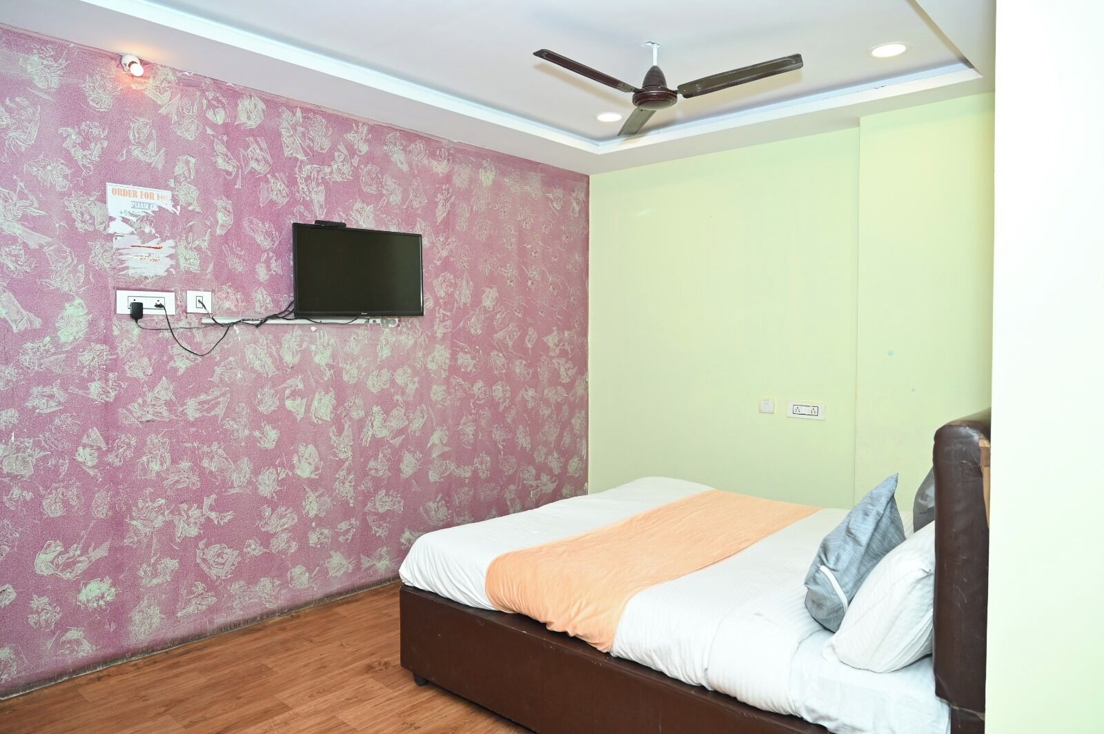 Ein Schlafzimmer mit Bett, Deckenventilator, wandmontiertem Fernseher und floralem Wandpapier.
