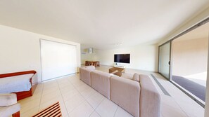 A modern living room with a sofa set, a TV, a dining area, and a sliding glass door.