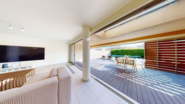A modern living room with a flat-screen TV, a sofa, and a dining area with a table and chairs.