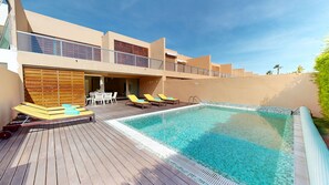 A poolside area with a wooden deck, lounge chairs, and a clear blue pool.
