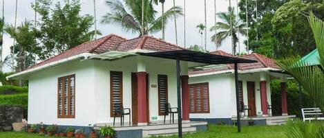 A two-story building with a red-tiled roof, white walls, and wooden shutters. There are steps leading to the entrance, and a covered porch area with chairs.