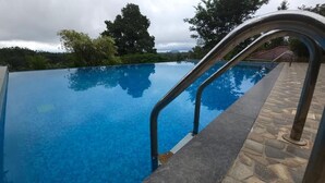 En klar, blå uendelig pool med sten trapper og metal gelændere, omgivet af frodig vegetation og træer.