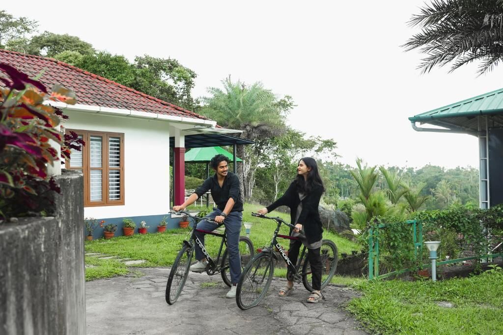 Deux personnes à vélo dans un jardin, avec une maison en arrière-plan.