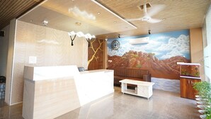 A reception area with a wooden reception desk, a white sofa, a small coffee table, and a mural of a mountainous landscape. - Hotel Star Inn (Jodhpur)