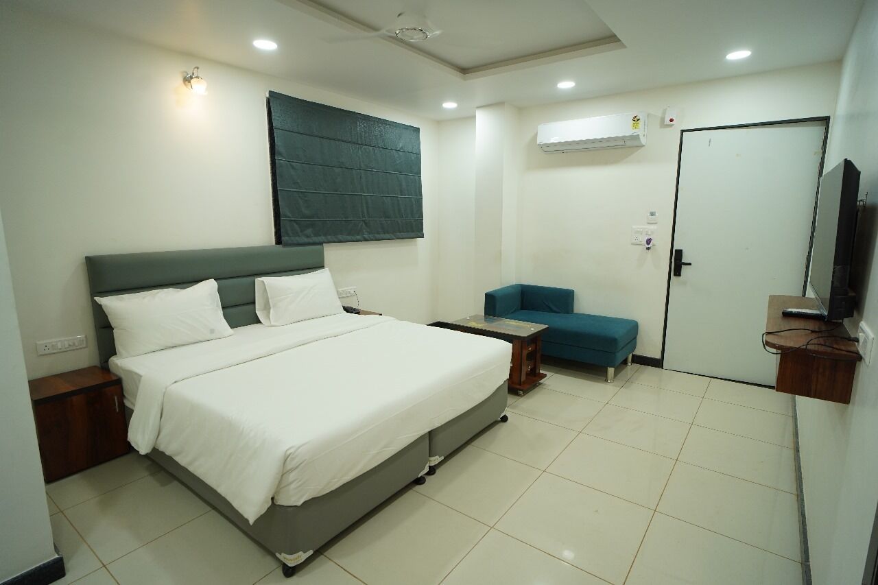 A hotel room with a large bed, a small seating area, a television, and an air conditioning unit.