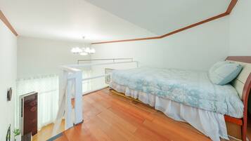 A bedroom with a bed, a wooden floor, a white railing, and a chandelier.