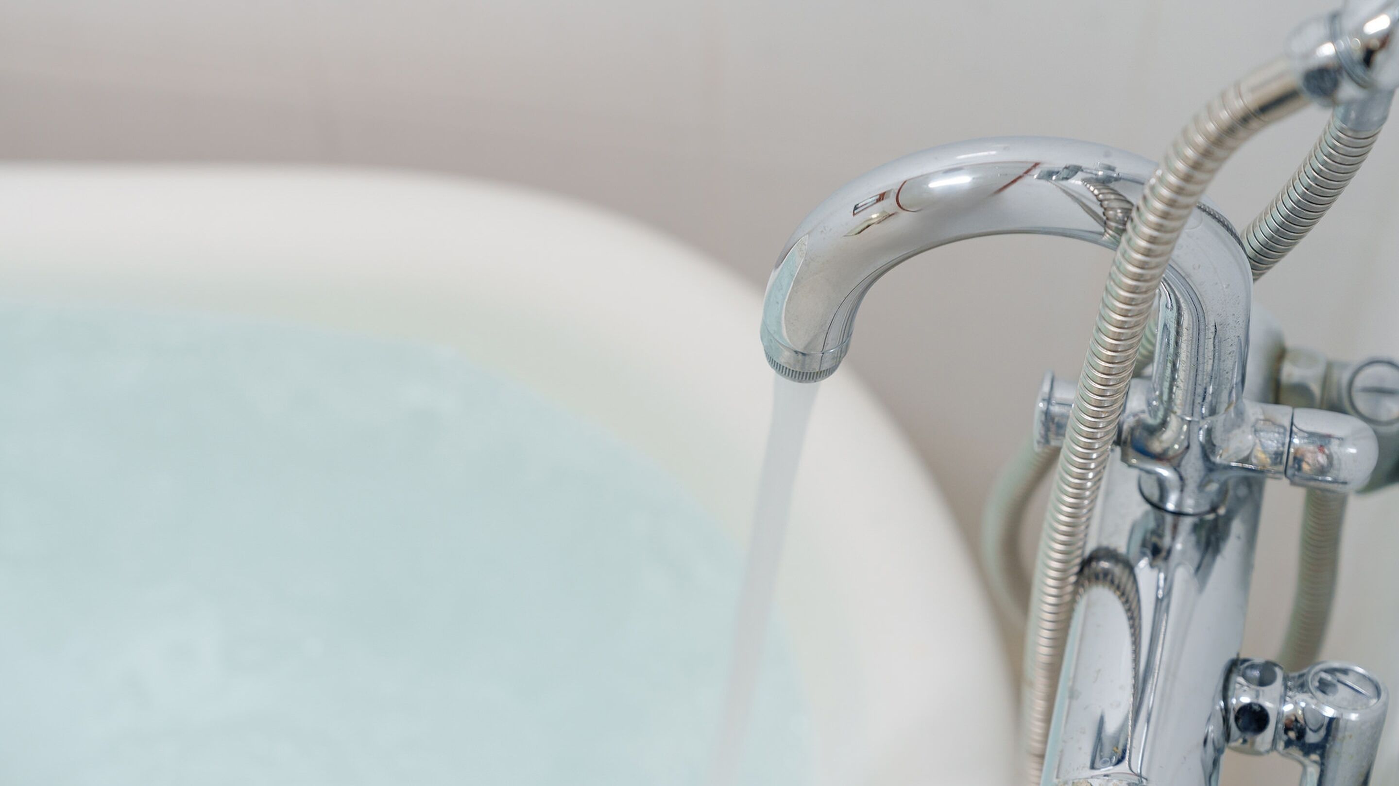 A close-up of a bathtub faucet with a shower head attached, water flowing from it.