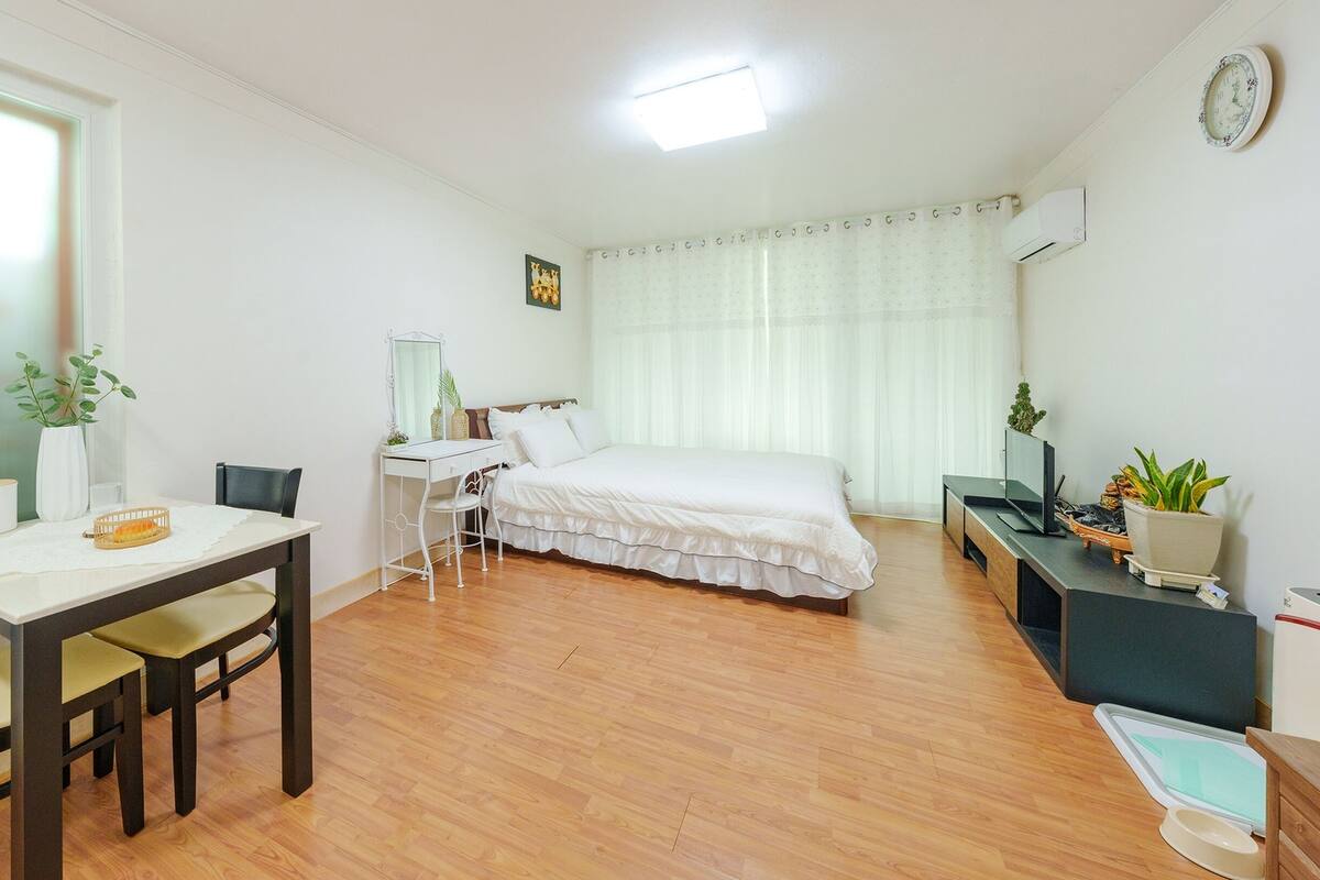 Un dormitorio con una cama, un escritorio, una silla, un espejo, una ventana y un televisor.