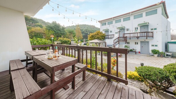 A wooden deck with a table and chairs, overlooking a courtyard with a building and greenery. - Taean Norabureo Pet Pension (Taean)