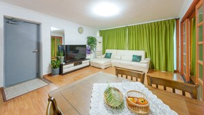 A living room with a sofa, a TV, a dining table with a placemat, and a green curtain. - Taean Norabureo Pet Pension (Taean)