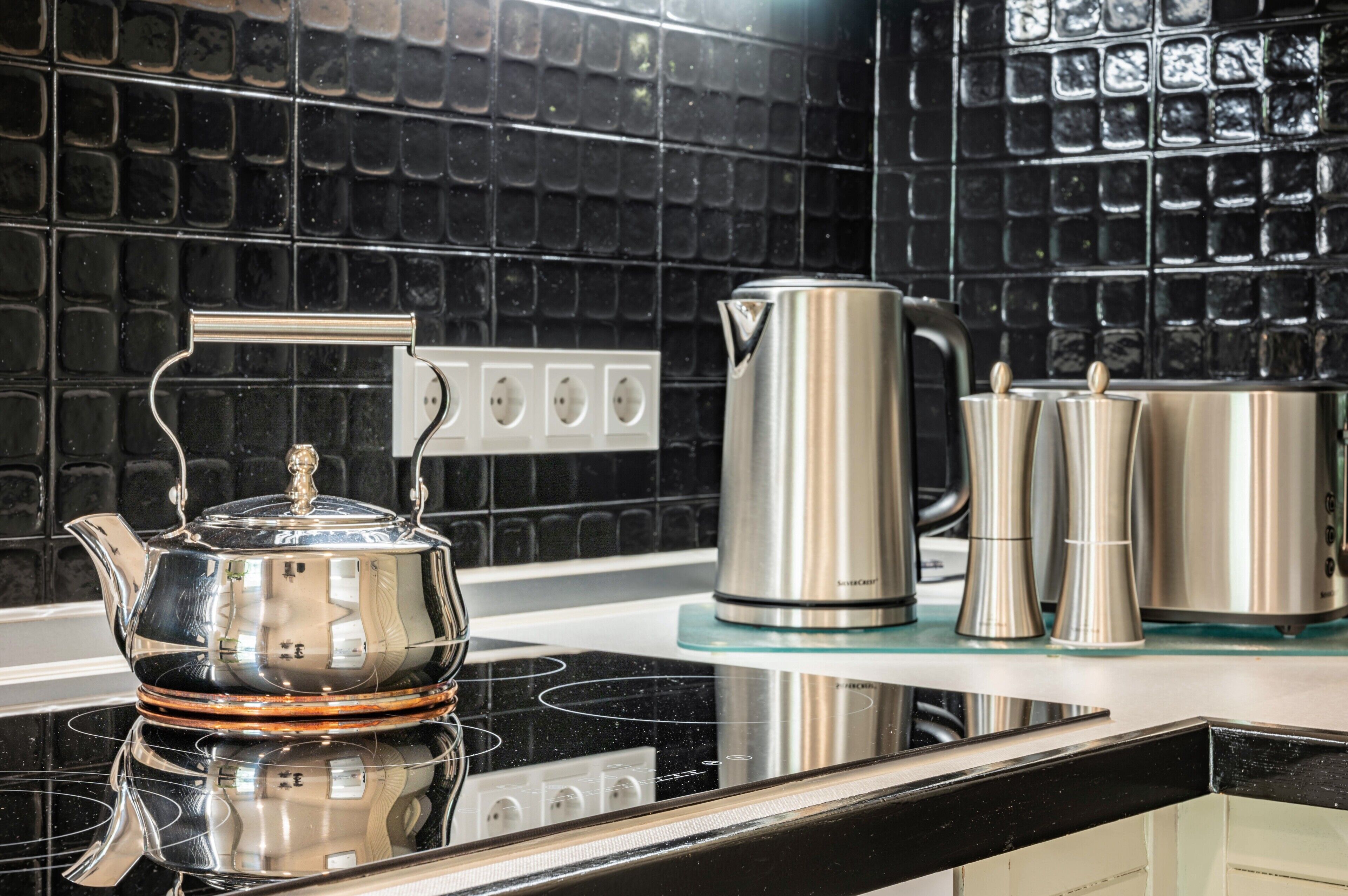 A kitchen with a black tiled backsplash, stainless steel appliances, and a reflective black countertop.