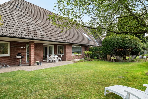 Ein Haus mit Ziegeldach, Backsteinfassade, überdachter Terrasse und Gartenmöbeln sowie einem gepflegten Rasen.
