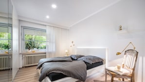 Een moderne slaapkamer met een groot bed, nachtkastjes, een stoel en een raam met jaloezieën.
