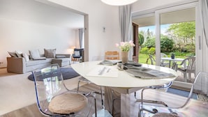 Een moderne woonkamer met een witte bank, een glazen salontafel en een eethoek met een witte tafel en stoelen.