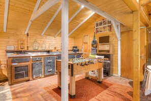 A cozy room with a wooden ceiling, a foosball table, a kitchen area, and a window with a view.