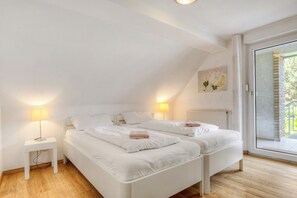 Une chambre avec deux lits, une table de chevet avec une lampe, un radiateur et une grande fenêtre donnant sur un beau paysage.