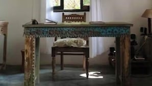Una habitación con una mesa de madera, una silla, una lámpara colgante y un ventanal con cortinas.
