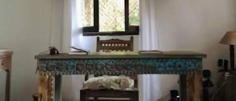Una habitación con una mesa de madera, una silla, una lámpara colgante y un ventanal con cortinas.
