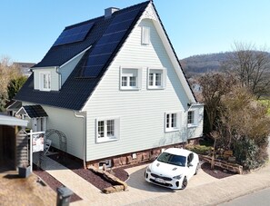 Una casa de dos pisos con paneles solares en el techo, un coche blanco estacionado adelante y un camino de piedra que conduce a la entrada.