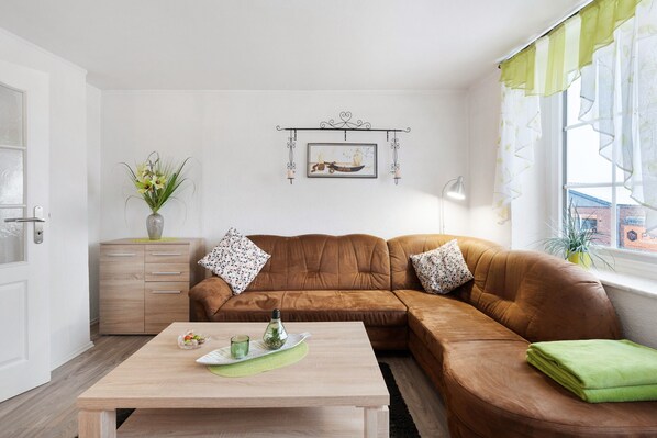Un salon avec un canapé en cuir marron, une table basse en bois, une décoration murale et une fenêtre avec des rideaux.