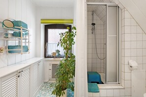 Une salle de bain équipée d’une douche, d’un lavabo, d’un miroir et d’une étagère où sont rangés les articles de toilette.