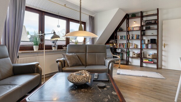 En stue med sofa, sofabord, lampe, reol og udsigt gennem et vindue.