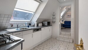 Et moderne køkken med ovenlys, hvide skabe, opvaskemaskine og mikrobølgeovn.