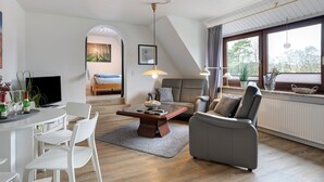 En moderne stue med spiseplads, sofa, fjernsyn og et stort vindue med gardiner.