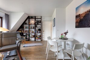 Una sala de estar con sofá, una mesa de comedor con sillas, una estantería y una escalera.