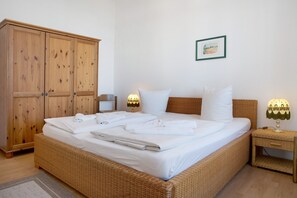 A neatly made bed with white linens, a wicker headboard, and a bedside lamp.