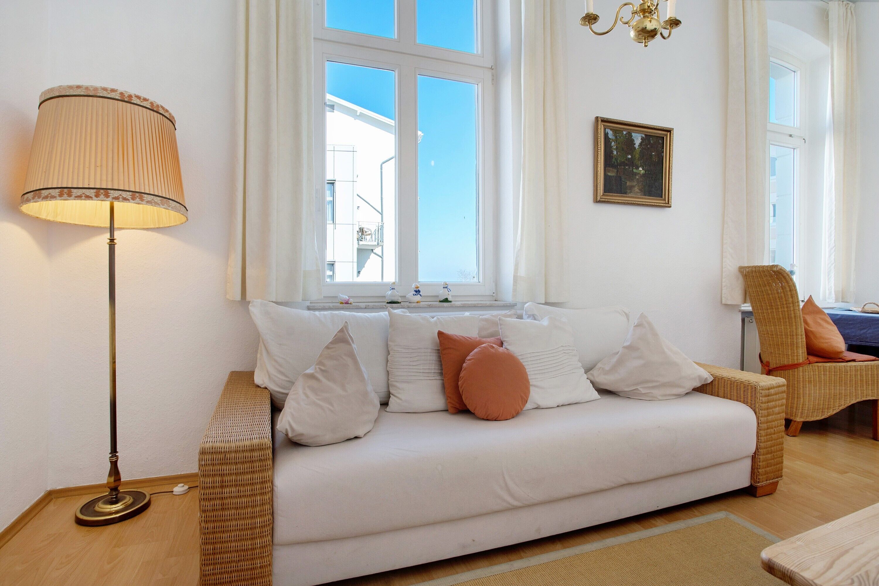 A living room with a sofa, a floor lamp, a wicker chair, and a window with a view.