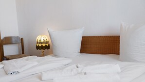 Ein ordentlich bezogenes Bett mit weißen Leinen, eine Lampe mit einer gemusterten Lampenschirm und ein Weiden-Kopfstück.