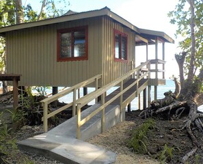 A wooden cabin with a concrete staircase leading up to a deck.