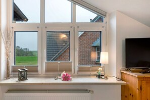 A room with large windows, a radiator, a television, and a small table with decorative items.
