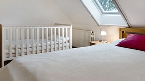 A room with a crib, a bed, a nightstand, a lamp, and a skylight. - Holiday Apartment Norderwurth (Büsumer Deichhausen)