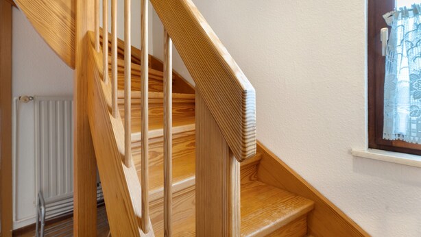 A wooden staircase with a handrail, a radiator, and a window with lace curtains. - Holiday Apartment Norderwurth (Büsumer Deichhausen)