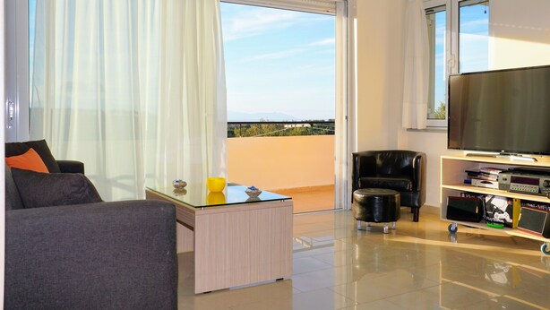 Un salon moderne avec un canapé, une table basse, un téléviseur posé sur un meuble et un balcon offrant une vue agréable.