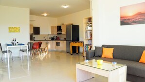 Un salon moderne avec une table basse en verre, un canapé gris agrémenté de coussins orange et une bibliothèque remplie de livres.